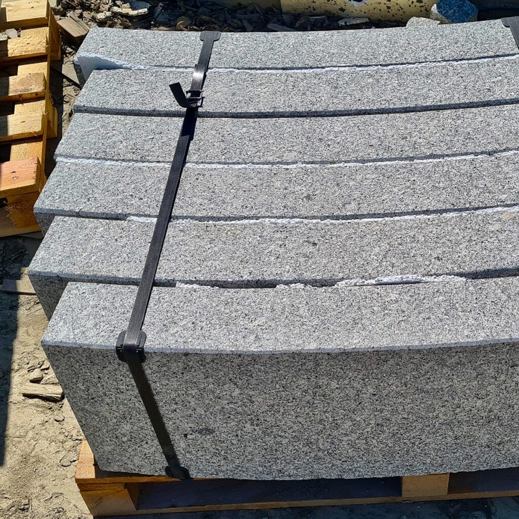 A collection of grey granite curved kerbs on pallets, highlighted by smooth, curved edges for added style