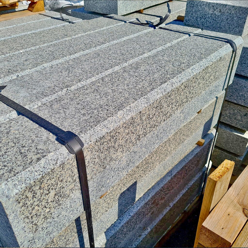 A stack of beveled grey granite kerbs resting on a wooden pallet, showcasing their textured surfaces and sturdy design