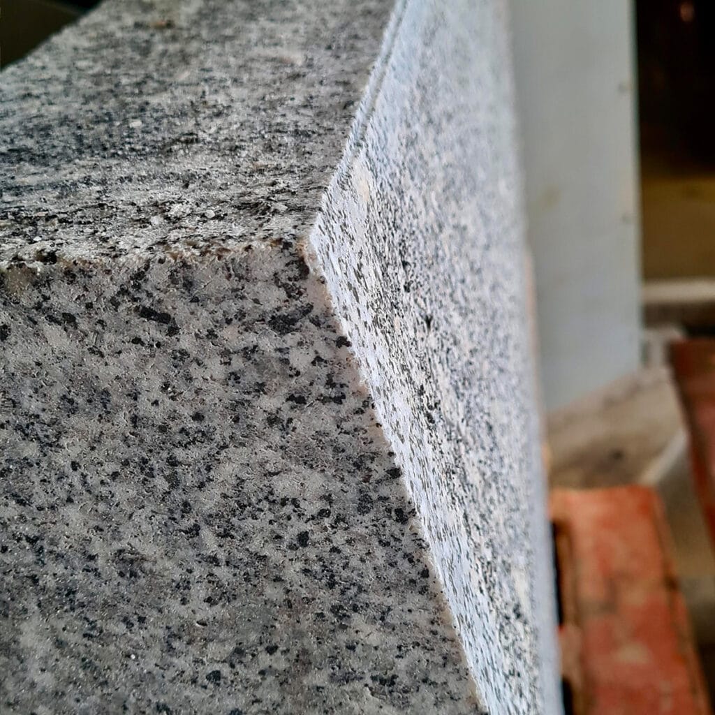 Close-up of a beveled granite kerb block against a clean white background, showcasing its texture and detail